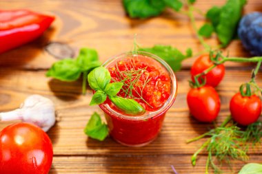 Sarımsaklı sebzelerle çevrili bir bardak domates sosu..