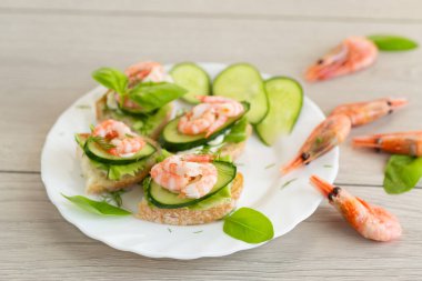 Tahta bir masanın üzerinde karides, marul ve salatalıklı mini kanepeler..