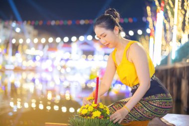 Loy Krathong Geleneksel Festivali, Tayland 'daki Loy Krathong kutlamalarında dolunay gecesi su tanrıçası için güzel bir Taylandlı kadın Krathong süsleme yaprağı tutuyor..