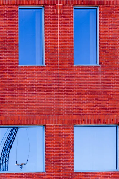 红砖建筑外墙 窗户反映蓝天 玻璃表面有扭曲的建筑用起重机 — 图库照片