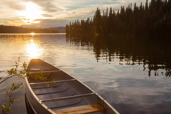 カナダのユーコン準州の人里離れた荒野にある美しいフランス人の湖の岸に縛り付けられたカヌー 湖を囲む北半球の森林タイガの上の日没 — ストック写真