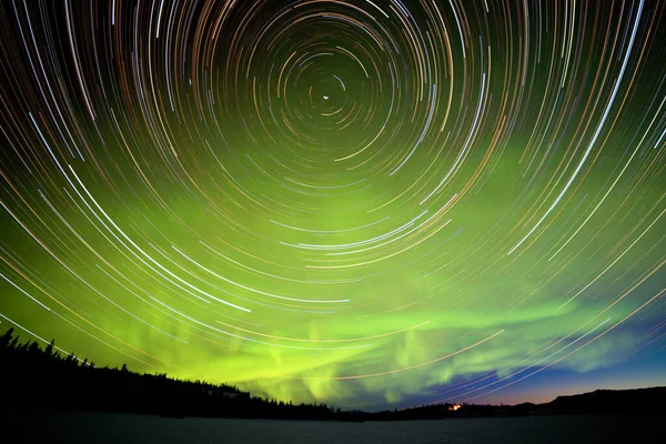 カナダのユーコン準州で夜明けの亀裂でオーロラやオーロラの緑色の輝くディスプレイを持つ天体写真の星の道 — ストック写真