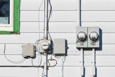 Elektrik besleme sayaçları ve telefon hattı bağlantı kutusunu konut evinin dış beyaz vinil kaplama duvarına bırakıyor.
