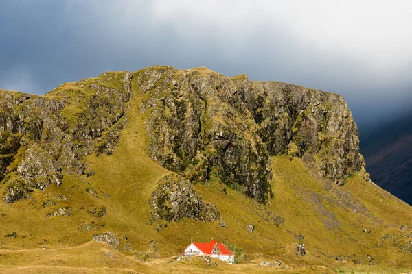 stock image Isolated farm house snuggled at base of huge rock cliff in barren green tundra landscape of East Iceland, Europe, EU