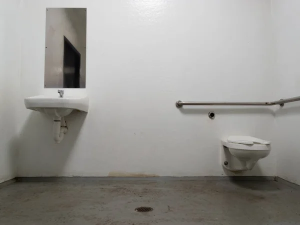 鏡と洗面台付きのシンプルなベアボーン公衆トイレと コンクリート床の上にトイレボウルを設置し 排水を簡単に清掃できます ストック画像