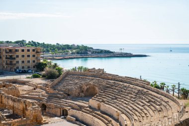 Wide-angle view of the ruins of the Roman amphitheater in Tarragona, built in the 2nd century AD, with the Mediterranean Sea in the background.