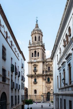 JAEN, SPAIN - 9 Mayıs 2022: Jaen Katedrali 'nin çan kulesi dar bir sokaktan görüldüğü gibi, İspanyol Barok şaheserlerinden biri, tesadüfen geçen insanlar.