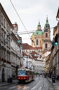 PRAG, CZECH Cumhuriyet - 24 AĞUSTOS 2022: Prag 'ın Mala Strana ilçesinde arka planda Aziz Nicholas Kilisesi' nin ortaya çıktığı bir caddede kırmızı tramvay.