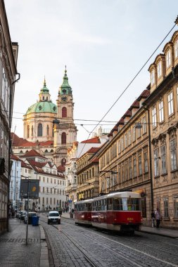 PRAG, CZECH Cumhuriyet - 24 AĞUSTOS 2022: Prag 'ın Mala Strana ilçesinde arka planda Aziz Nicholas Kilisesi' nin ortaya çıktığı bir caddede kırmızı tramvay.