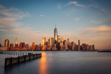 Manhattan siluetinin uzun bir görüntüsü Hoboken, New Jersey 'den alacakaranlıkta görülüyor. Sakin akşam ışığı şehrin Hudson Nehri üzerindeki ikonik gökdelenlerini güçlendiriyor..