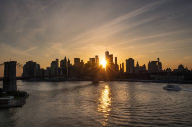 Brooklyn Köprüsü ve New York, yoğun bir günbatımının altında, Doğu Nehri boyunca ufuk çizgisi.