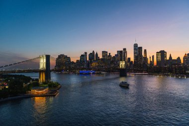 Brooklyn Köprüsü ve New York, yoğun bir günbatımının altında, Doğu Nehri boyunca ufuk çizgisi.