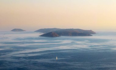 A solitary boat sailing in the Ria de Pontevedra in Galicia at dusk, with the serene Ons Islands in the background. clipart