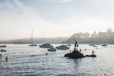 SANXENXO, SPAIN - 11 AĞUSTOS 2023: İspanya 'nın Rias Baixas kentindeki sisli bir yaz gününde Sanxenxo' daki Silgar plajına demirlemiş banyo ve küçük tekne siluetleri.