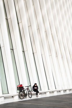 NEW YORK CITY - MAY 18, 2024: A lone rider rests with his bike under the imposing form of the Oculus, the architectural landmark for the new World Trade Center Transportation Hub in Lower Manhattan, New York City. clipart