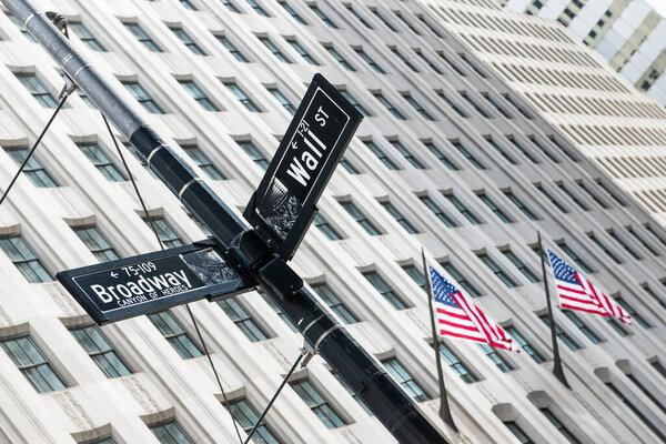 Wall Street and Broadway street signs with American flags waving in the background, captured in Manhattan, New York City, USA