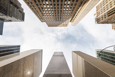 Manhattan, New York 'taki modern gökdelenlerin alçak açılı görüntüsü. Bu dramatik perspektif, New York şehrinin dinamik enerjisini ve etkileyici ufuk çizgisini yakalayarak şehrin çağdaş mimarisinin yüksek yüksekliğini ve parlak tasarımını vurgular..