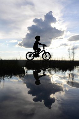 Child on a bicycle on the edge of a lake with its reflection in the water clipart