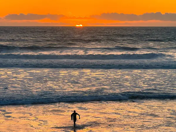 Surfer Kommt Bei Sonnenuntergang Aus Dem Wasser lizenzfreie Stockbilder