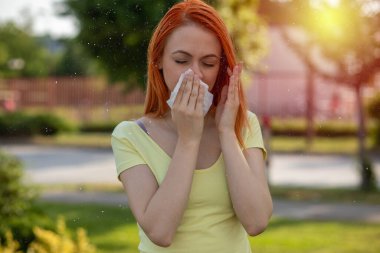 Alerji yüzünden burnunda sorun var! Genç kızıl saçlı kadın çiçek açan ağacın önünde hapşırıyor. Polen alerjisi belirtileri