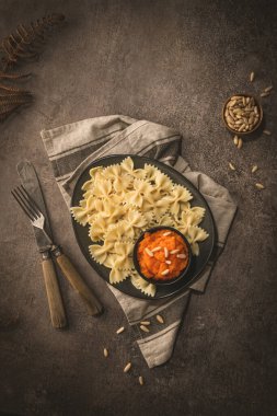 Seramik tabakta Farfalle makarna, kabak püresi ve küçük bir seramik kasede çam fıstığı, siyah taş mutfak tezgahında..