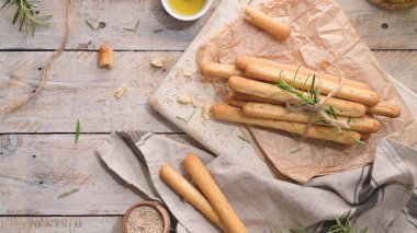 Traditional italian breadsticks grissini with rosemary, olive oil and sesame seeds on wooden countertop.