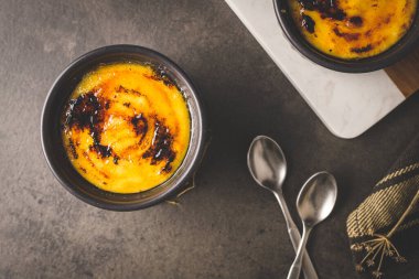 Creme brulee. Üzerinde karamelli şeker, kaşıklar, koyu kırsal masa olan Fransız vanilyalı tatlı kaseleri..
