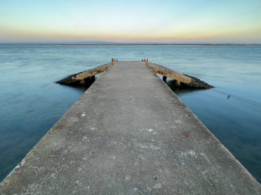 Portekiz 'deki Ria de Aveiro' ya boş beton iskele, dramatik gökyüzü ve sakin su.