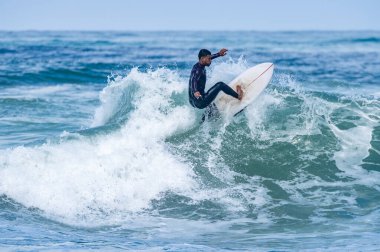 Portekiz, Furadouro Sahili 'nde sörf yapan bir sörfçü. Okyanusta dalgaları yakalayan adamlar. Su sörfü sporu. İnsanlar yaz tatilinde su sporları dersleri ve plaj yüzme aktiviteleri yapar..
