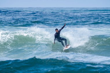 Portekiz, Furadouro Sahili 'nde sörf yapan bir sörfçü. Okyanusta dalgaları yakalayan adamlar. Su sörfü sporu. İnsanlar yaz tatilinde su sporları dersleri ve plaj yüzme aktiviteleri yapar..