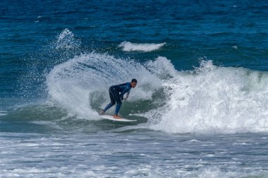 Portekiz, Furadouro Sahili 'nde sörf yapan bir sörfçü. Okyanusta dalgaları yakalayan adamlar. Su sörfü sporu. İnsanlar yaz tatilinde su sporları dersleri ve plaj yüzme aktiviteleri yapar..
