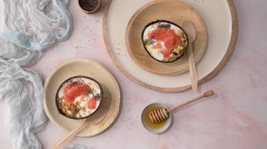 Yogurt with grapefruit, granola, chia and honey served in half a coconut shell on a rose marble kitchen countertop.