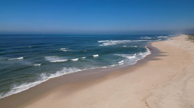 Kumlu sahil antenine çarpan dalgaların yan görüntüsü. Yukarıdan gelen boş bir sahile çarpan okyanus dalgalarının kuş bakışı görüntüsü..