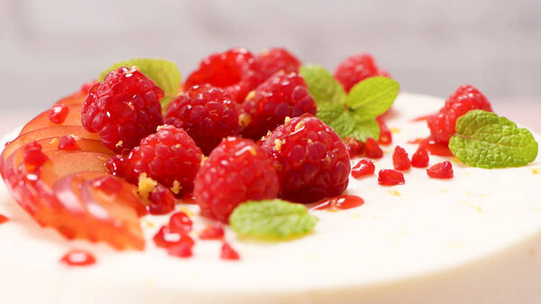 Cheesecake with fresh raspberries, plums and mint leaves.
