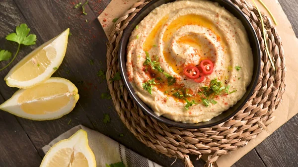 Seramik kasede nefis humus. Siyah ahşap arka planda renkli abur cubur kompozisyonu.