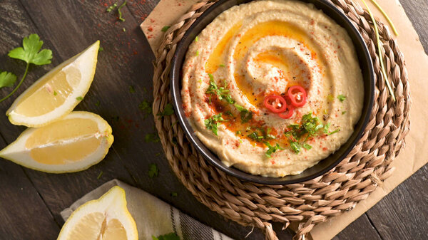 Delicious hummus in ceramic bowl. Colorful snack composition on a black wooden background.