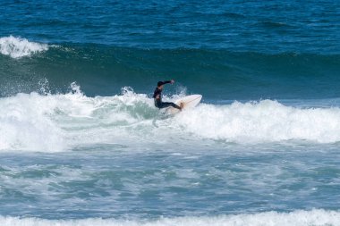 Portekiz, Furadouro Sahili 'nde sörf yapan bir sörfçü. Okyanusta dalgaları yakalayan adamlar. Su sörfü sporu. İnsanlar yaz tatilinde su sporları dersleri ve plaj yüzme aktiviteleri yapar..