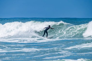 Portekiz, Furadouro Sahili 'nde sörf yapan bir sörfçü. Okyanusta dalgaları yakalayan adamlar. Su sörfü sporu. İnsanlar yaz tatilinde su sporları dersleri ve plaj yüzme aktiviteleri yapar..