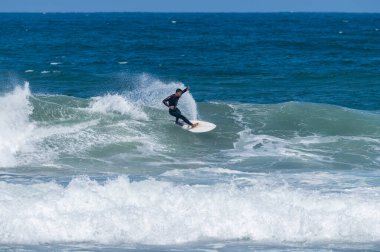 Portekiz, Furadouro Sahili 'nde sörf yapan bir sörfçü. Okyanusta dalgaları yakalayan adamlar. Su sörfü sporu. İnsanlar yaz tatilinde su sporları dersleri ve plaj yüzme aktiviteleri yapar..