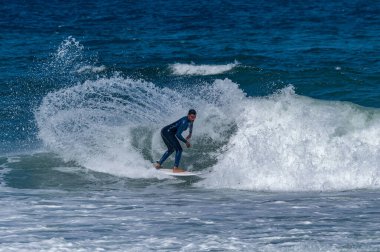 Portekiz, Furadouro Sahili 'nde sörf yapan bir sörfçü. Okyanusta dalgaları yakalayan adamlar. Su sörfü sporu. İnsanlar yaz tatilinde su sporları dersleri ve plaj yüzme aktiviteleri yapar..