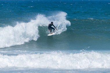 Portekiz, Furadouro Sahili 'nde sörf yapan bir sörfçü. Okyanusta dalgaları yakalayan adamlar. Su sörfü sporu. İnsanlar yaz tatilinde su sporları dersleri ve plaj yüzme aktiviteleri yapar..