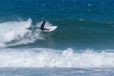 Portekiz, Furadouro Sahili 'nde sörf yapan bir sörfçü. Okyanusta dalgaları yakalayan adamlar. Su sörfü sporu. İnsanlar yaz tatilinde su sporları dersleri ve plaj yüzme aktiviteleri yapar..