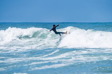 Portekiz, Furadouro Sahili 'nde sörf yapan bir sörfçü. Okyanusta dalgaları yakalayan adamlar. Su sörfü sporu. İnsanlar yaz tatilinde su sporları dersleri ve plaj yüzme aktiviteleri yapar..