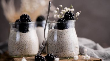 Böğürtlenli Chia pudingi, karanlık bir masada cam kavanozlarda üç porsiyon..