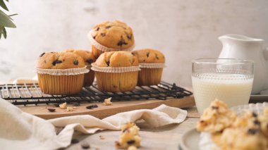 Chocolate chip muffins with milk served on glass cups on white kitchen countertop.