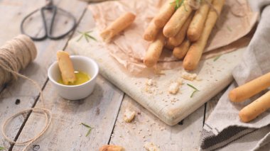 Traditional italian breadsticks grissini with rosemary, olive oil and sesame seeds on wooden countertop.