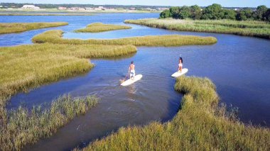 Erkek ve kadın hava görünümünü paddleboarding göl kenarında ayakta. Genç çift su sporları göl kenarında yapıyoruz. Erkek ve kadın turist mayo yaz tatili vardır..