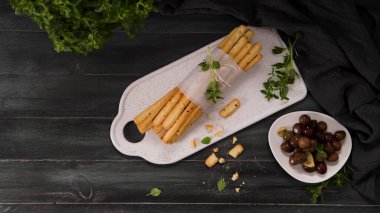 Taze pişmiş ev yapımı Grissini ekmek çubukları beyaz seramik tepside ve mutfak tezgahının üzerinde zeytinyağı ve fesleğen otu ile.