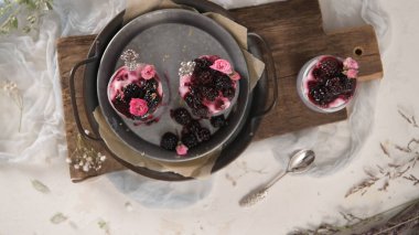 Böğürtlenli Chia pudingi, beyaz bir masada cam kavanozlarda üç porsiyon.