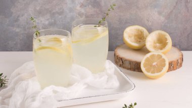 Soğuk limonata veya alkollü kokteyl limon, biberiye ve hafif bir arka plan üzerinde cam bardaklarda buz ile.